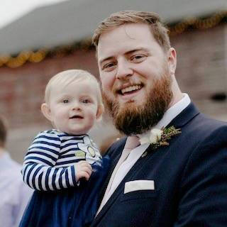 Darin Douglass wearing a suit, holding a baby
